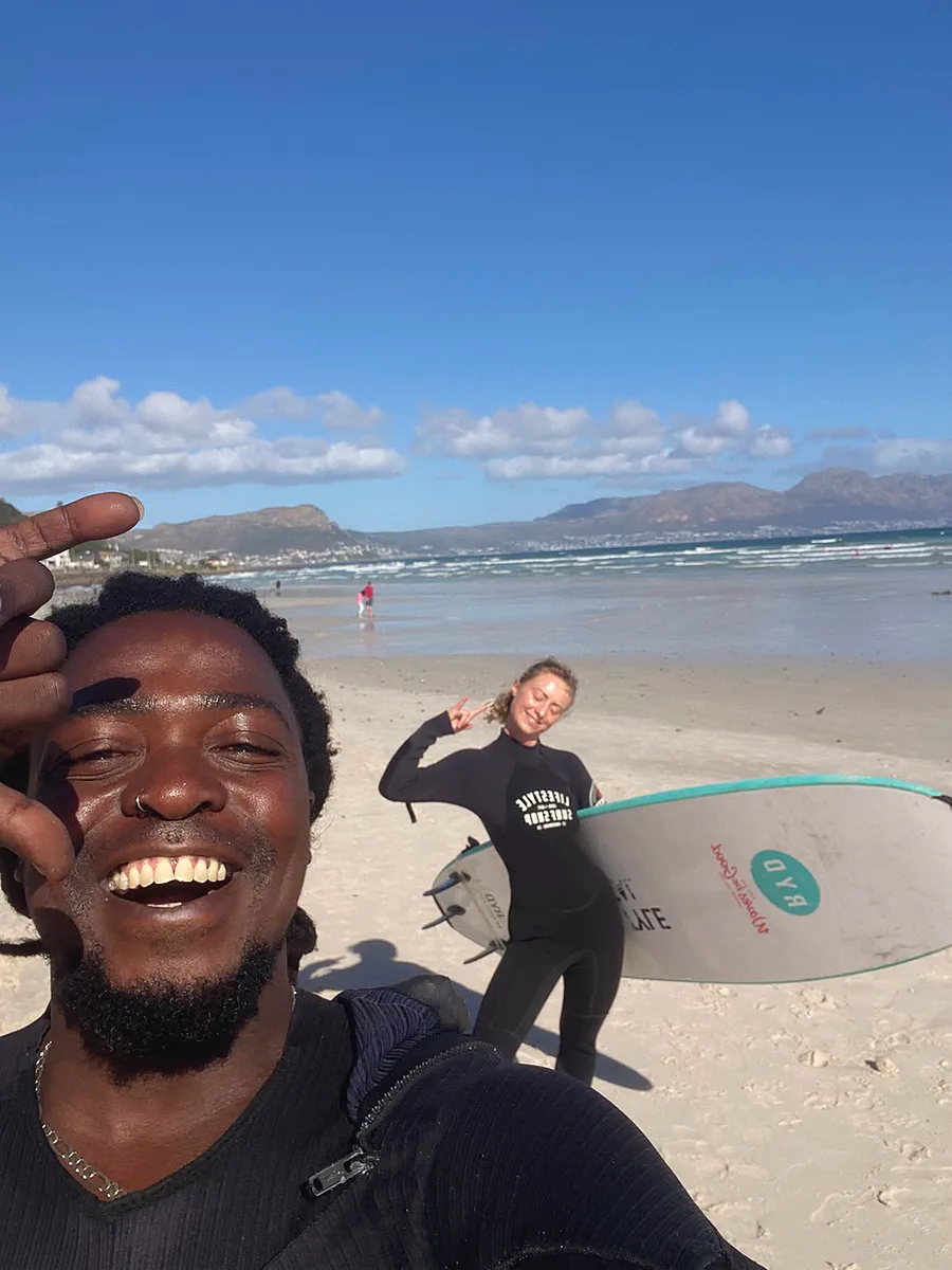 Kwezi and a student on the beach after a lesson, the False Bay mountains behind